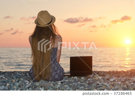Girl in a hat sits on the beach, near laptop. Sea 37286465