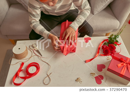 A man wrapping gifts in red ribbon and fresh roses A man wrapping gifts in red ribbon and fresh roses 37290470