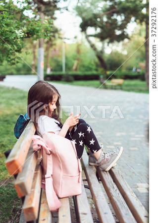 little girl with a smartphone sitting on a bench little girl with a smartphone sitting on a bench 37292176