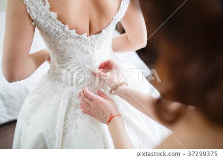 Bridesmaid is helping the bride to dress 37299375