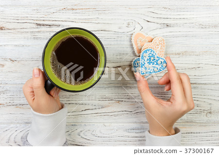 Female hands with coffee and heart shaped cookies Female hands with coffee and heart shaped cookies 37300167