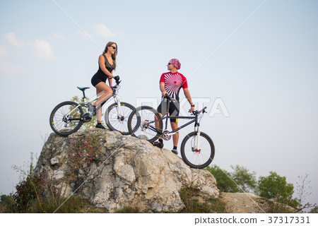 Couple standing with bicycles on the rock under evening sky 37317331