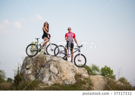Couple standing with bicycles on the rock under evening sky Couple standing with bicycles on the rock under evening sky 37317332