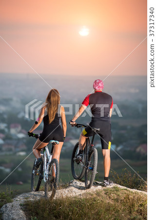 Couple bicyclist with mountain bikes on the hill at sunset Couple bicyclist with mountain bikes on the hill at sunset 37317340