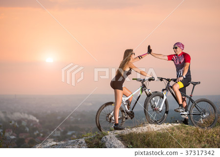 Cyclist couple with mountain bikes on the hill at sunset 37317342