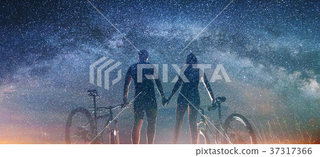 Couple cyclists with mountain bikes at night under starry sky 37317366