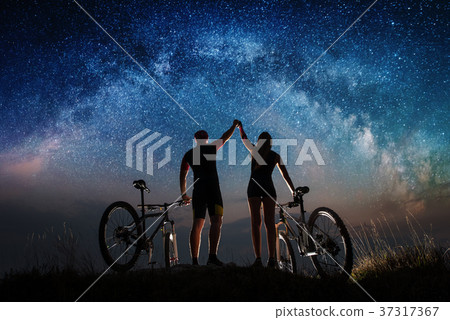 Couple cyclists with mountain bikes at night under starry sky 37317367