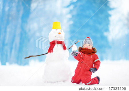 Little boy in red winter clothes having fun with snowman in snowy park Little boy in red winter clothes having fun with snowman in snowy park 37325206