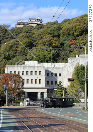 運行在縣政廳和市政廳前面的Botchan火車有鬆山城堡的在背景中 運行在縣政廳和市政廳前面的Botchan火車有鬆山城堡的在背景中 37337276