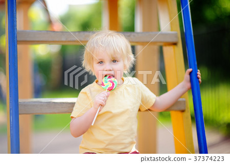 Little boy having fun and eating big lollipop on outdoor playground Little boy having fun and eating big lollipop on outdoor playground 37374223