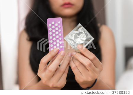 Asian woman holding condom and birth control pills Asian woman holding condom and birth control pills 37380333