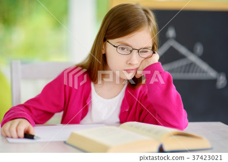 Stressed and tired schoolgirl studying with a pile of books on her desk Stressed and tired schoolgirl studying with a pile of books on her desk 37423021