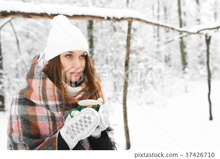 girl in a white hat wrapped in a rug holds a mug  37426710