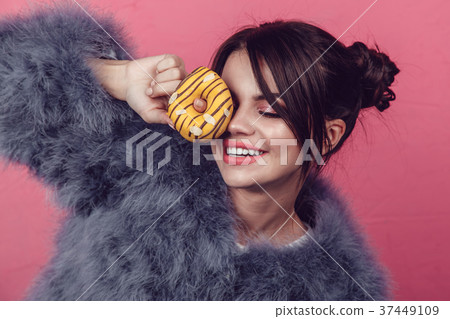 Beautiful girl in a fur coat with donuts in hands Beautiful girl in a fur coat with donuts in hands 37449109