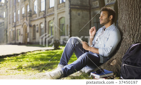 College student sitting with notebook under tree College student sitting with notebook under tree 37450197
