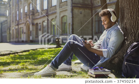 Young male in headphones sitting on grass, leaning Young male in headphones sitting on grass, leaning 37450214