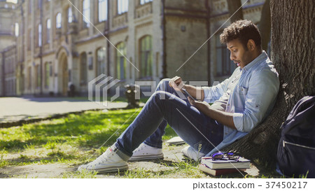Surprised guy sitting under tree, using mobile Surprised guy sitting under tree, using mobile 37450217