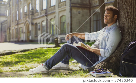 Multiracial guy sitting under tree, looking and Multiracial guy sitting under tree, looking and 37450340