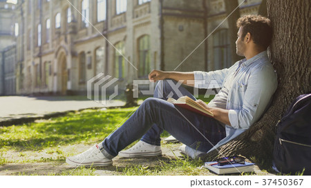 Multinational guy sitting under tree with book 37450367
