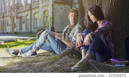 Two young people sitting under tree, girl looking Two young people sitting under tree, girl looking 37450472
