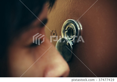 Closeup of woman looking through peephole 37477419