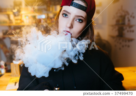 Young pretty woman in red cap smoke an electronic Young pretty woman in red cap smoke an electronic 37499470