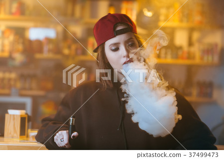 Young pretty woman in red cap smoke an electronic Young pretty woman in red cap smoke an electronic 37499473