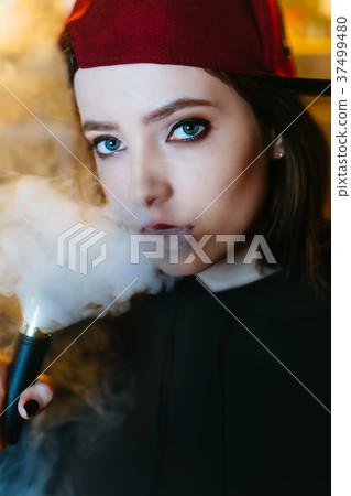 Young pretty woman in red cap smoke an electronic 37499480