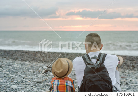 Young father and son are sitting on the beach 37510901