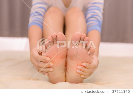 Young woman massaging her feet on the bed 37511540