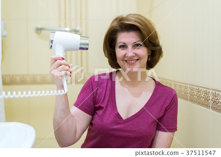woman dries hair a hair dryer in a bathroom woman dries hair a hair dryer in a bathroom 37511547