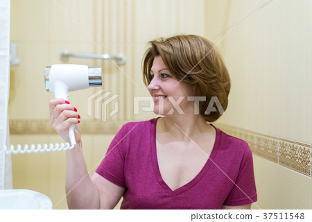 woman dries hair a hair dryer in a bathroom 37511548