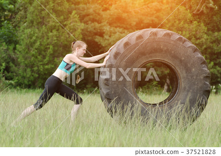 Girl in sportswear is pushing tire. Street workout Girl in sportswear is pushing tire. Street workout 37521828