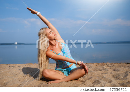Blonde girl in a blue suit is doing yoga on beach 37556721