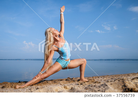 Blonde girl in a blue suit is doing yoga on beach Blonde girl in a blue suit is doing yoga on beach 37556739