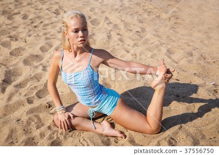 Blonde girl in a blue suit is doing yoga on beach Blonde girl in a blue suit is doing yoga on beach 37556750