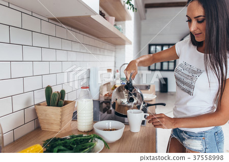 Woman pouring boiling water into a cup from kettle Woman pouring boiling water into a cup from kettle 37558998