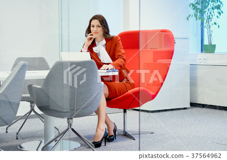 businesswoman sitting on a red chair in a glass office and works businesswoman sitting on a red chair in a glass office and works 37564962