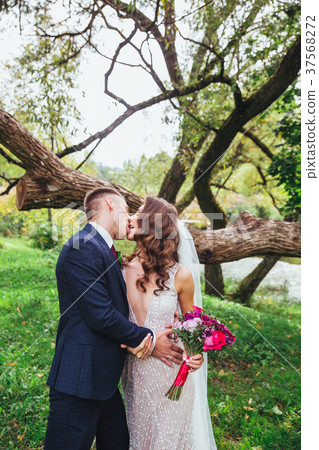 Beautiful newlywed bride and groom kissing in park Beautiful newlywed bride and groom kissing in park 37568272
