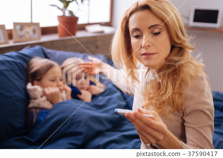 Troubled mother taking her childrens temperature Troubled mother taking her childrens temperature 37590417