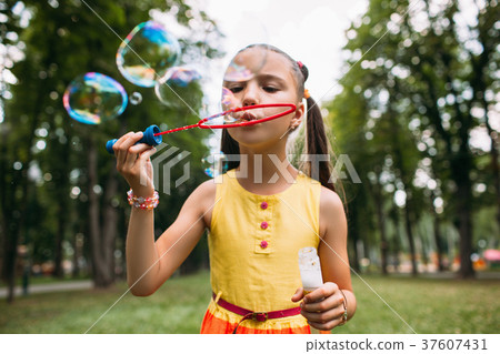 Rapt little girl blows bubbles in the park. Rapt little girl blows bubbles in the park. 37607431