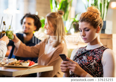 woman with smartphone and friends at restaurant 37615255
