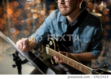 man with guitar writing to music book at studio 37615414