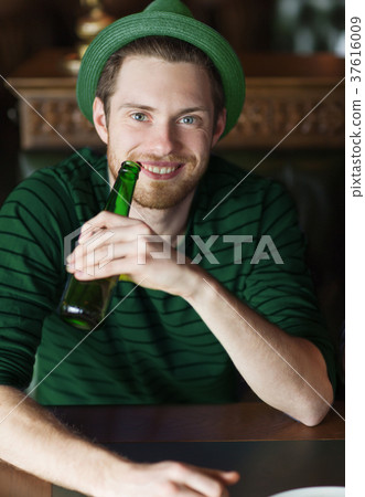 man drinking beer from green bottle at bar or pub 37616009