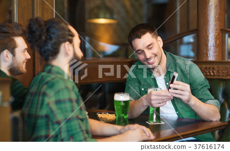 friends with smartphone drinking green beer at pub 37616174