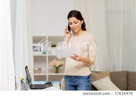 woman with papers calling on smartphone at home 37616476