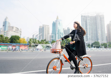 Asian office lady riding bicycle through urban area 37627152