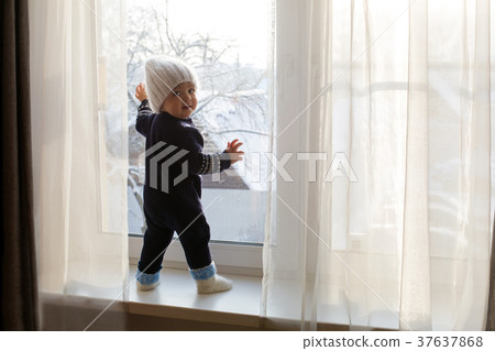 child in a warm blue jumpsuit is on window in 37637868