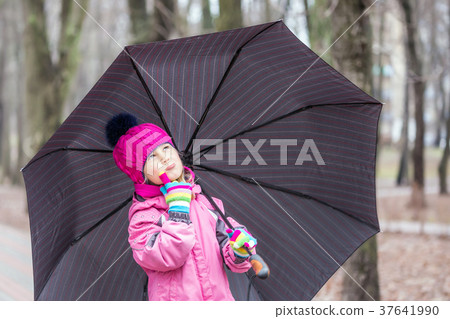 Little girl walking under umbrella in a park Little girl walking under umbrella in a park 37641990