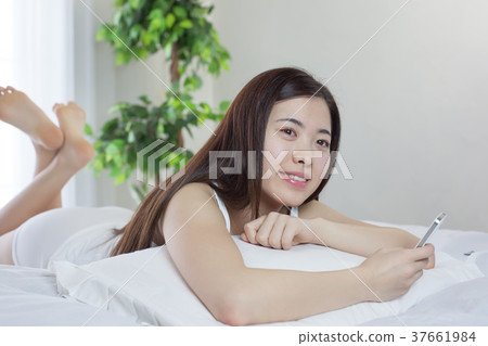 Young woman operating a smartphone with a bed Young woman operating a smartphone with a bed 37661984